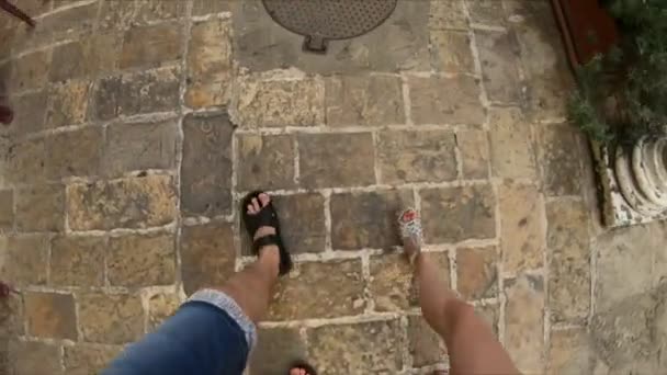 Pernas masculinas e femininas caminham ao longo da calçada estreita da rua. Viagem turística, Viagem. Lente Fisheye disparada. Estrada de pedra. Humor romântico, Férias — Vídeo de Stock