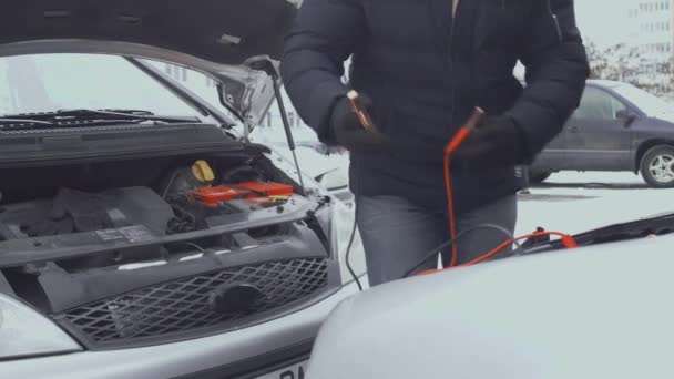 Людина з'єднує кабелі минперів з поштовим терміналом автомобільної батареї. Худ або капелюх, піднятий взимку вдень на парковці. Несправності або проблеми з автомобілем. Частина 3 — стокове відео