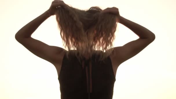 Κορίτσι σηκώνει σγουρά υπέροχα μαλλιά της στο φόντο ενός ηλιόλουστου ηλιοβασιλέματος, κοντινό πλάνο, αργή κίνηση — Αρχείο Βίντεο