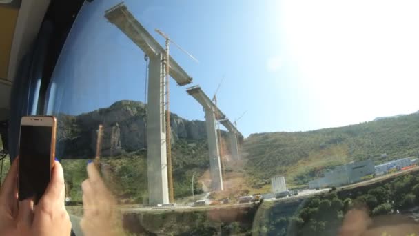 Uitzicht vanuit het raam van een toeristische bus. Bouw van een hoogmoderne brug in Montenegro tussen canyons, slow motion — Stockvideo