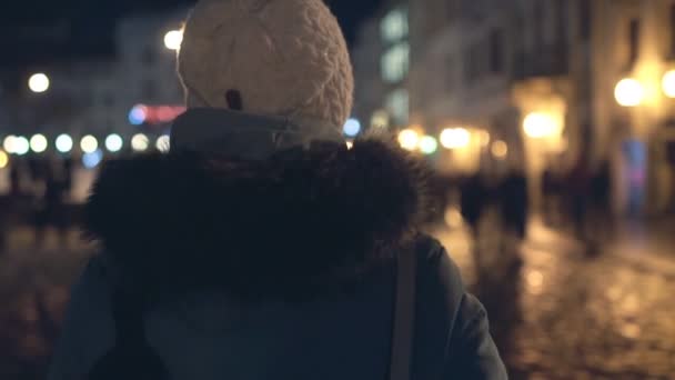 Une fille marche à travers une ville festive de nuit dans laquelle les lumières sont allumées, arrière-plan. Espace de copie, ralenti — Video