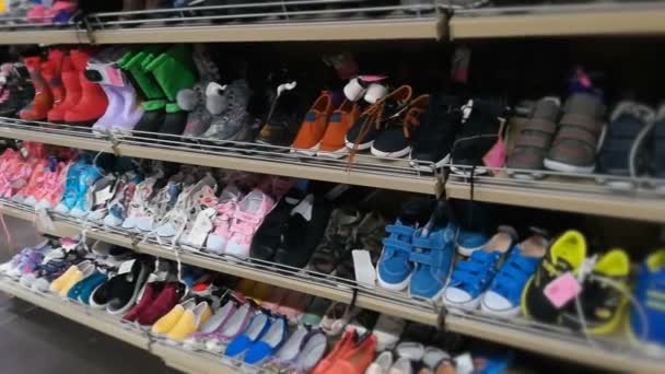 El estante con calzado para niños, niñas y niños en la tienda. Zapatos para niños, zapatillas y botas de varios colores en el centro comercial o hipermercado — Vídeos de Stock