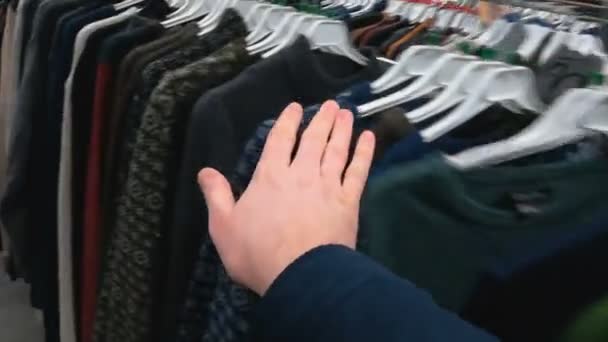 Pullover selectie. Truien ophangen. Hand kiest nieuwe nette mannelijke kleding in het winkelcentrum of de winkel. Inspectie alvorens diverse gekleurde truien in de supermarkt te monteren. Close-up eerste persoon bekijken schot — Stockvideo