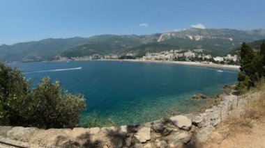 Budva yakınlarındaki Becici kasabasının sahil şeridi manzarası. Karadağ, tatil köyü plajı. Tekne gezisi. Arka planda oteller ve dağlar, yavaş çekim