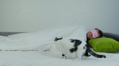 Kedi yavaşça yatağın karşısına geçiyor ve battaniyenin altında yatan yatağın sahibinin yanına oturuyor. Yeşil yastığa uzanmış pembe gözlü beyaz beyaz beyaz bir adam.