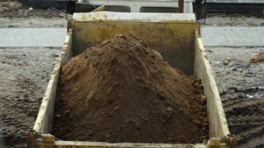 Zaman çizelgesi kazıcı, alışveriş merkezi binasının bir aşaması sırasında çöp kamyonuna kum ve farklı kargolar boşaltıyor. En üstten görüntüle