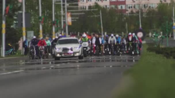 Hromadná jízda na kole ve městě. Cyklistický maraton. Policejní auto s blikajícími světly doprovází kolonu sportovců. Závodní závod pro cyklisty. Občané jezdí na kole na hlavní ulici. Široký záběr — Stock video