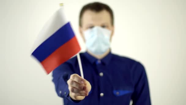 Een man met een beschermend masker op zijn gezicht tegen het virus dat zwaait met de vlag van het land Rusland. Land Coronavirus Disease Concept, COVID-2019, pandemie — Stockvideo