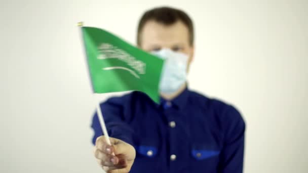 Ένας άντρας με προστατευτική μάσκα στο πρόσωπό του ενάντια στον ιό κουνώντας τη σημαία της χώρας της Σαουδικής Αραβίας. Country Coronavirus Disease Concept, COVID-2019, πανδημία — Αρχείο Βίντεο