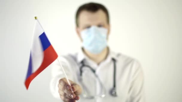 Man dokter met een beschermend masker zwaaiend met de vlag van Rusland op een witte achtergrond. Land coronavirus epidemie concept — Stockvideo