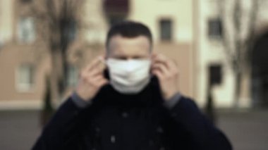 Odak dışı, bulanık. Koronavirüs salgını sırasında beyaz maske takan bir adam COVID-19 kullanıyor çünkü ülke karantina altında. Sars salgını, mercov-2. Kişi koruyucu ekipman takar