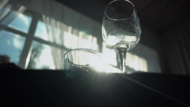 A glass of wine and glass glasses stand on the table against the background of the sun shining through the window. Serving table for the holiday, celebration — Stock Video