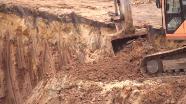 Una excavadora cava tierra arcillosa en un pozo de cimentación para construir una fundación. Cubo de hierro excavadora con tierra, fondo, industria — Vídeos de Stock