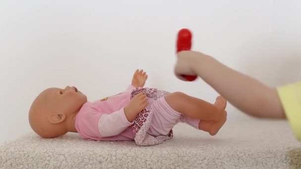 Uma menina brinca com uma boneca, e com um pequeno martelo neurológico, atinge o joelho da boneca. Conceito de neurologia infantil, verificação reflexa, espaço de cópia — Vídeo de Stock