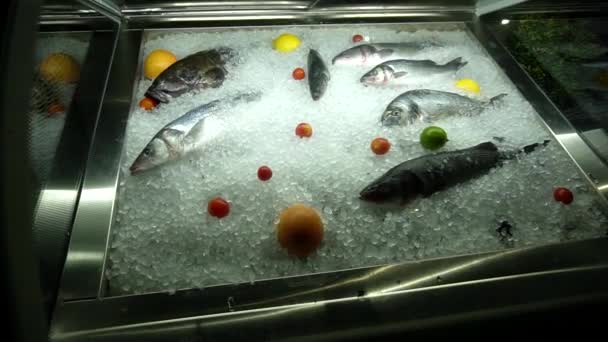 Заморожена риба з льодом лежить на вітрині магазину з овочами та фруктами. Продаж природної та здорової риби в магазинах, копіювання простору — стокове відео