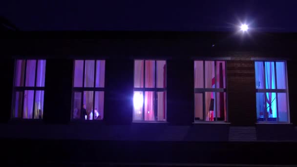 Vista desde la calle hasta el edificio donde los jóvenes pasan el rato en la discoteca. La luz de las ventanas del edificio en el que tiene lugar la celebración, la noche, la unión — Vídeo de stock