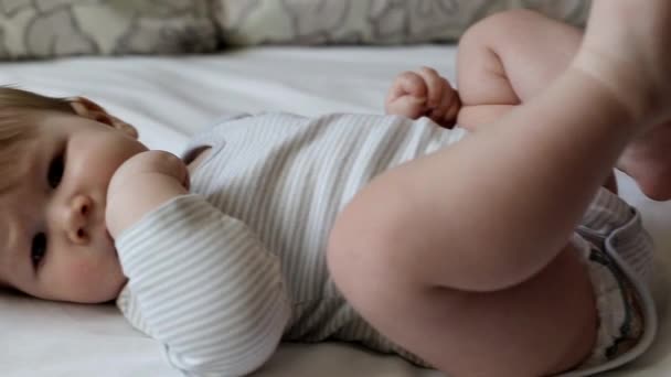 Petit beau garçon aux grands yeux. Le bébé s'allonge sur le lit et joue. Âge environ un an, arrière-plan, caucasien — Video