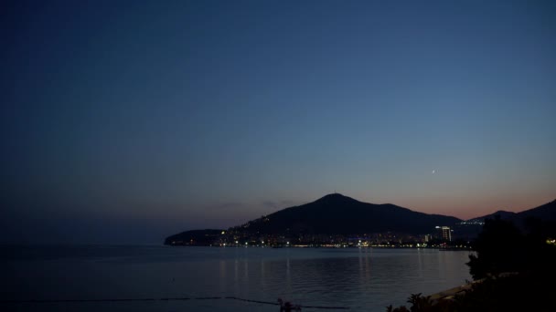 Schöner Berg vor dem Hintergrund des Nachthimmels mit dem Mond. Nacht Stadt leuchtet mit Lichtern, das Meer, Kopierraum, Urlaub — Stockvideo