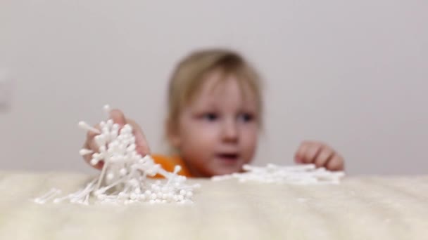 小さな美しい女の子は、耳やスキンケア、コピースペース、綿をきれいにするためのテーブルから綿の芽を取ります — ストック動画