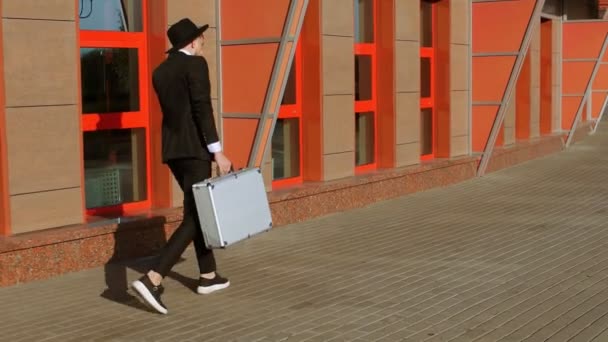 Man wearing black suit and hat with silver case walks outside to meeting to transfer money. Corruption and bribery concept. Businessman looks like Jew or Italian mafia is talking on smartphone. — Stock Video