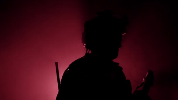 A military soldier in modern outfit with weapons is standing in the smoke in the studio. Military conflict concept, back light, shadow. Slow motion — Stock Video