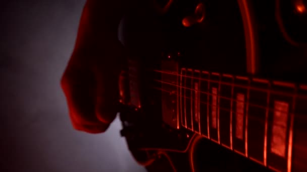 Um homem toca os dedos da guitarra e as cordas de perto. Iluminação de palco multi-colorido, fundo, câmera lenta — Vídeo de Stock