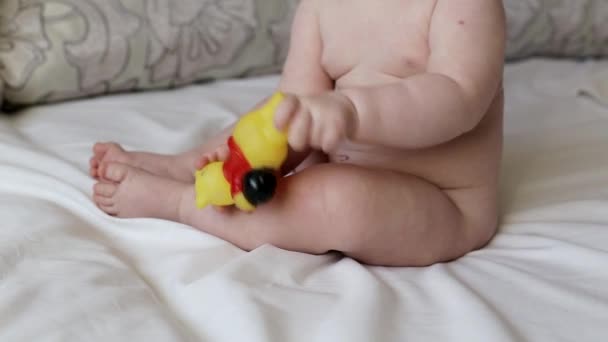 Голый пухлый мальчик играет с игрушкой на кровати, крупным планом — стоковое видео