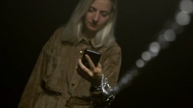 Kafkasyalı genç bir kız elinde bir akıllı telefon tutuyor ve içine bakıyor, eline metal bir zincir bağlanıyor. Yeni teknolojiler ve sosyal ağlar rehine konsepti, siyah arka plan, yavaş çekim