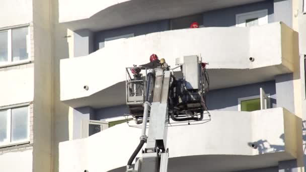 Повітряна платформа пожежної машини піднімає пожежників у захисному кошику для гасіння пожежі в багатоповерховій багатоповерхівці, пожежник — стокове відео