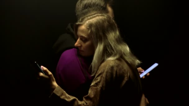 Любящие парень и девушка обнимаются и смотрят на смартфоны. Концепция заложников социальных сетей и Интернета, фон, технологии — стоковое видео