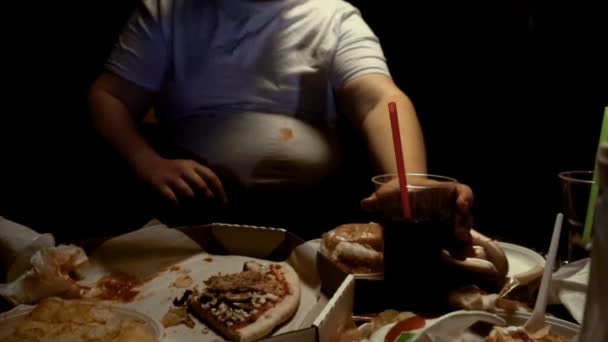 Толстяк ест нездоровую пищу и пьет газировку, смотрит телевизор дома. Чревоугодие и лишний вес, еда заложников, замедленная съемка, ожирение — стоковое видео