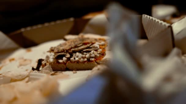 A piece of pizza in a box and a plate with leftovers of food is on the table. The concept of malnutrition of harmful and fatty foods, slow motion — Stock Video