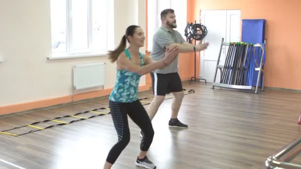 Die junge schöne Trainerin ist mit einem jungen Mann mit Bart, der übergewichtig ist, in Fitness verstrickt. Gesunder Lebensstil — Stockvideo