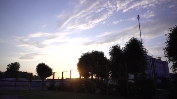 Hermoso amanecer en el patio de recreo de la ciudad. El sol naranja sale de detrás de árboles verdes, verano, fondo, paisaje — Vídeos de Stock