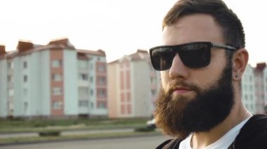 Siyah gözlüklü, sakallı, vahşi adamın portresi. Şık bir adam gün batımında ağır çekimde duruyor. Kulağında küpe olan modaya uygun biri. Şık, modaya uygun. Sabit çekim