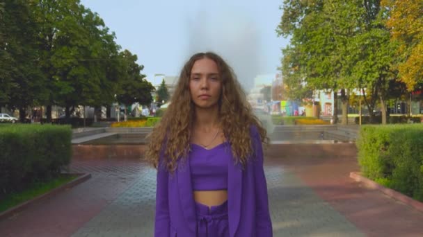 Retrato de linda imagen caucásica rizado chica de pelo largo en un traje sin maquillaje. La mujer a la moda de estilo se queda quieta en cámara lenta. La elegante dama de moda está en el parque. Vogue hembra mira en una cámara — Vídeo de stock