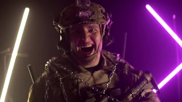 A military caucasian soldier in camouflage uniform and a helmet with a weapon laughs at the camera. Military action, background, slow motion — Stock Video