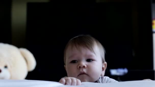 Маленький эмоциональный белый мальчик младенец смотрит в камеру с карими большими глазами, на заднем плане — стоковое видео