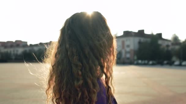 Curly long haired girl without makeup turns and looks into camera. Fashionable stylish woman stands still in slow motion. Trendy fancy lady is in central square. Vogue female model. Natural beauty — Stock Video