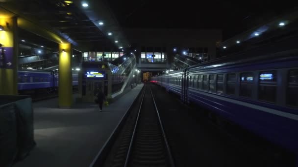 El tren sale de la estación de tren de pasajeros por la noche. Vista desde la parte trasera de la ventana del último vagón sobre raíles en movimiento. Concepto de viajes y turismo. El tren se aleja — Vídeo de stock