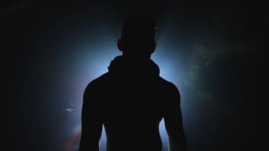 Genç bir erkek dansçı bir ışık kaynağına karşı karanlıkta dans ediyor. Kaslı vücudu ve zarafeti olan seksi bir adam.
