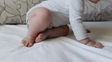 Kalın bacaklı küçük bir çocuk. Yatakta, arka planda, 7 aylık.