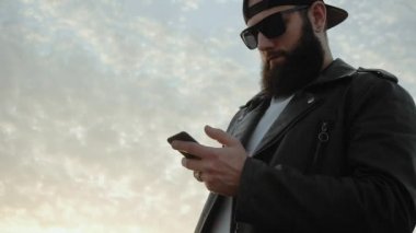 Sakallı vahşi adam akıllı telefona bakıyor ve haberleri izliyor. Adam internetten sipariş veriyor ve ödeme yapıyor. İletişim. Şık bir adam parmaklarını ekranda gezdiriyor. Uzaktan Gönderme