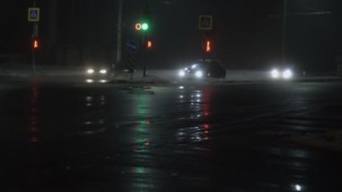 Arabalar, araçlar, trafik ışıklarıyla kavşağı otomatikman geç. Kışın sisli bir gece şehri. Islak asfalta yansıyor. Farlardan gelen ışık. Puslu ya da sisli, yol trafiği için kötü görüş mesafesi, kötü hava