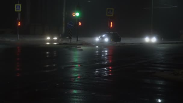 Bilar, fordon, kör förbi korsningen med trafikljus. Nattstad i dimma på vintern. Reflektion över våt asfalt. Ljus från strålkastare. Dimma eller dimma, dålig sikt för vägtrafiken, dåligt väder — Stockvideo