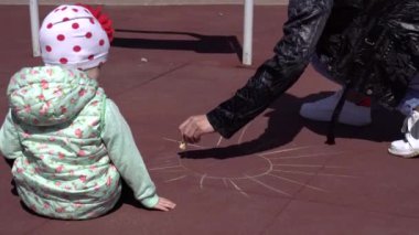 Küçük kız oyun bahçesinde annesiyle oynuyor renkli pastel boyalarla resim çiziyor, arka planda, mutlu.