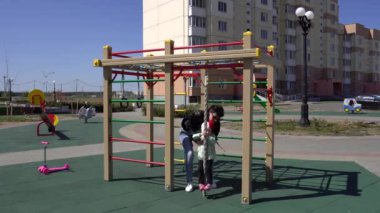 Neşeli beyaz bir kız annesiyle yeni bir oyun parkında oynuyor. Mutlu ve mutlu bir aile