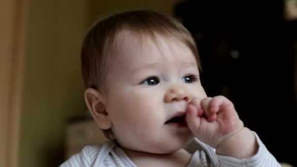 Piccolo bel ragazzo con grandi occhi marroni succhia il dito e distoglie lo sguardo. Età circa un anno — Video Stock