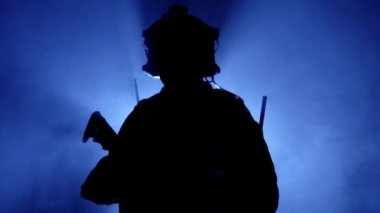 Askeri teçhizatlı asker. Mavi arka planda ateşli bir silah var. Arka plan, askeri operasyonlar. Amerikan ordusu, ağır çekim.
