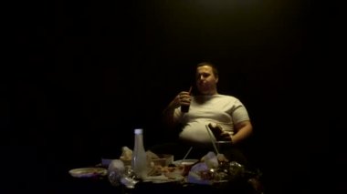 Şişman adam abur cubur yiyor, hamburger yiyor, sosisli yiyor, televizyon seyrediyor, ağır çekimde, kilolu.